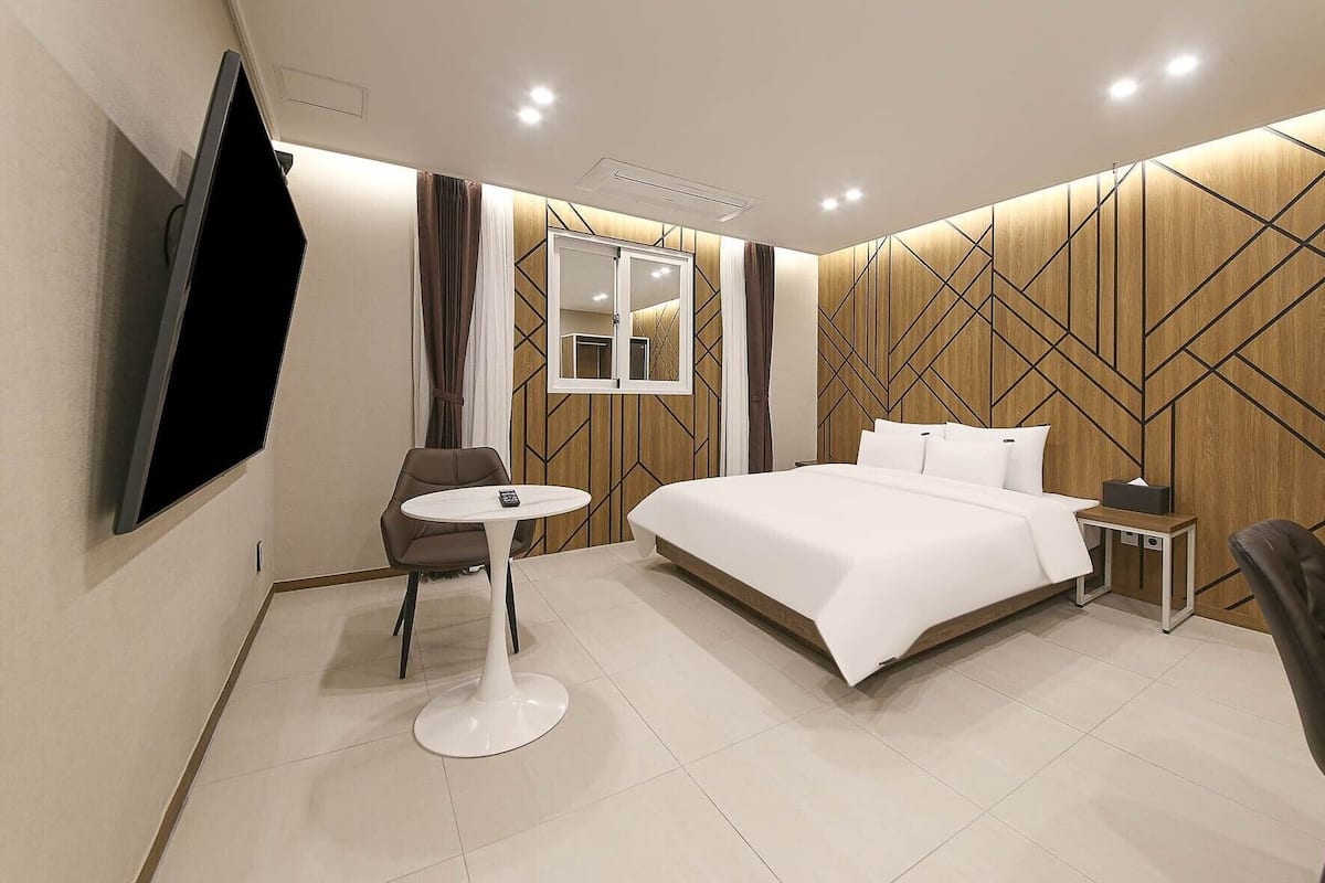 Habitación de hotel moderna con una cama grande, un televisor montado en la pared, una mesita redonda y una silla.