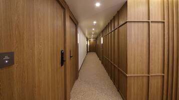 Un couloir aux murs recouverts de lambris en bois et doté d’un revêtement de sol en moquette, qui mène à une porte au fond.