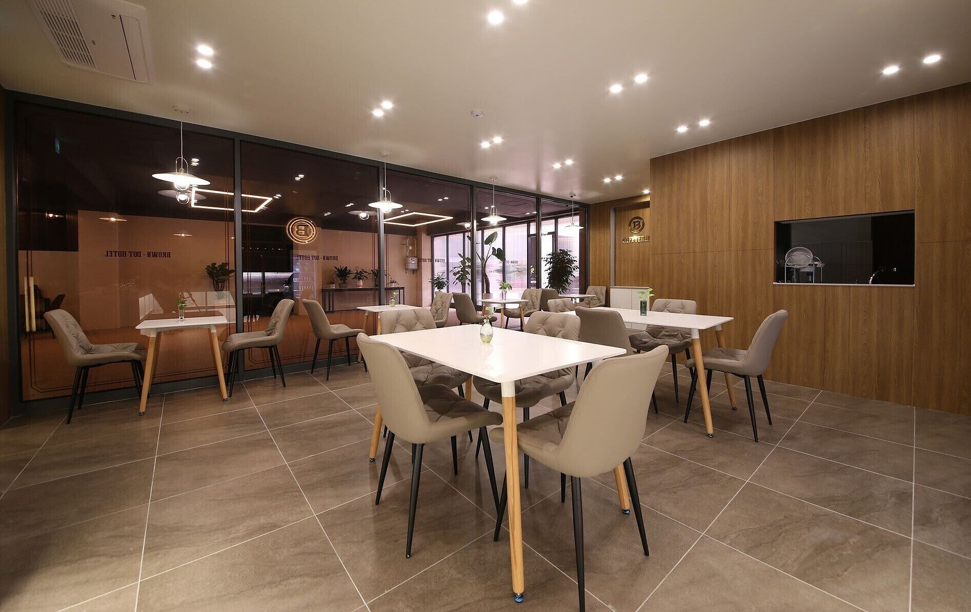 A modern dining area with multiple tables and chairs, a wooden accent wall, and a large window with plants.