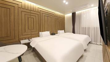 A hotel room with two beds, a small table, and a wooden panel wall.