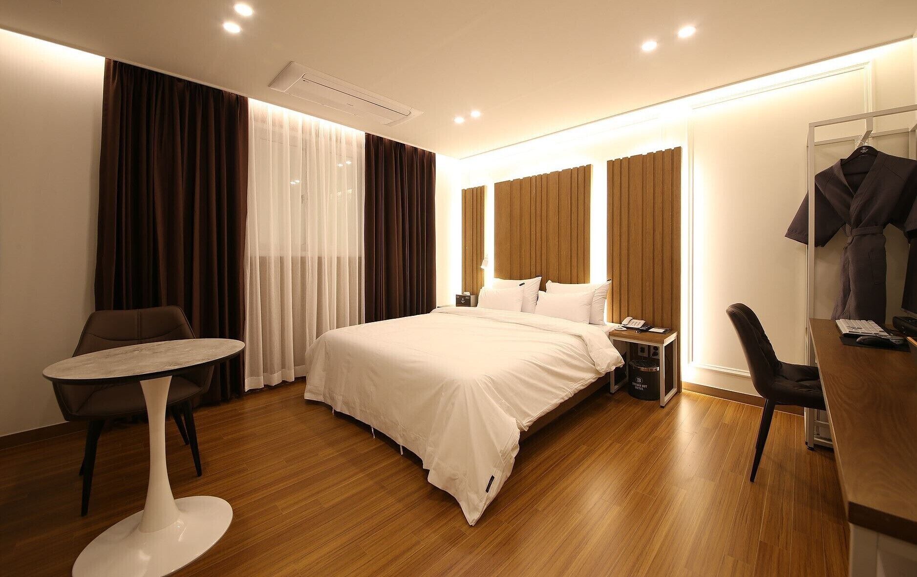 Una habitación de hotel moderna con una cama grande, una mesita redonda, un escritorio con una silla y un armario.