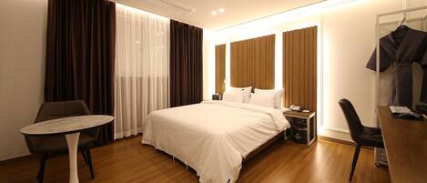 Una habitación de hotel moderna con una cama grande, una mesita redonda, un escritorio con una silla y un armario.