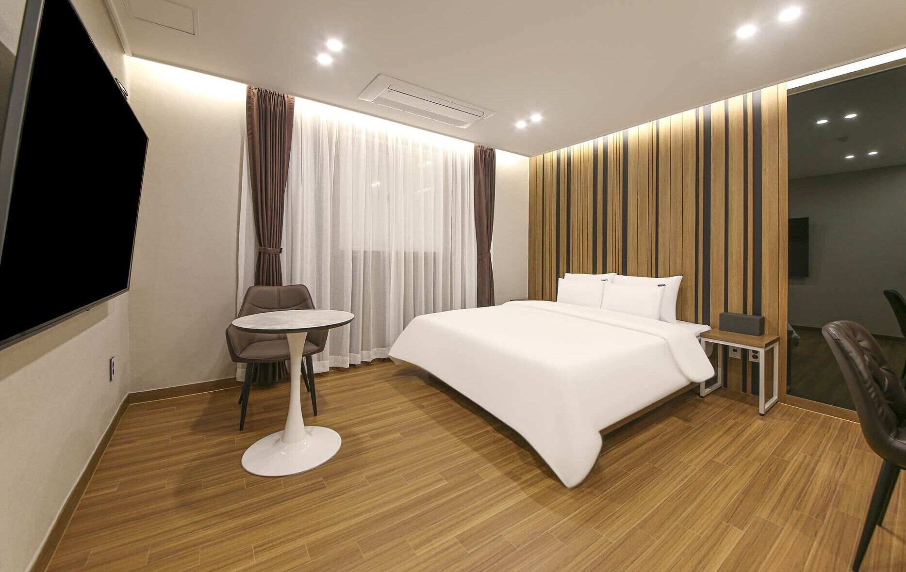 A modern hotel room with a large bed, a small round table, a chair, and a TV.