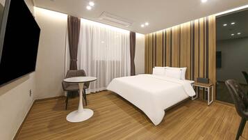 Ein modernes Hotelzimmer mit einem großen Bett, einem kleinen runden Tisch, einem Sessel und einem Fernseher.