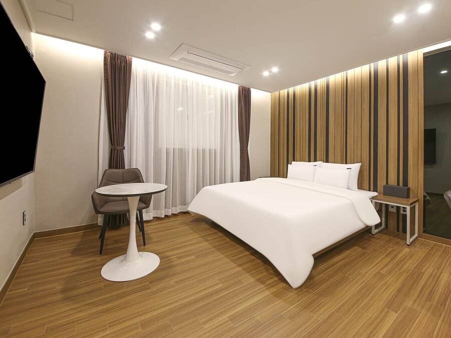 Ein modernes Hotelzimmer mit einem großen Bett, einem kleinen runden Tisch, einem Sessel und einem Fernseher.