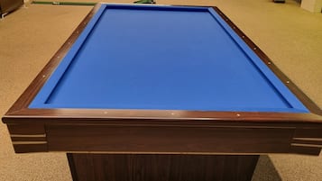 A pool table in a room with a carpeted floor and a ceiling with linear light fixtures.
