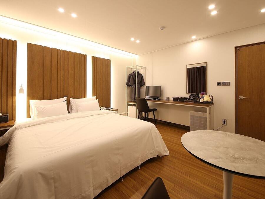 Una habitación de hotel con una cama grande, un escritorio con computadora, una silla, una mesita y un armario.