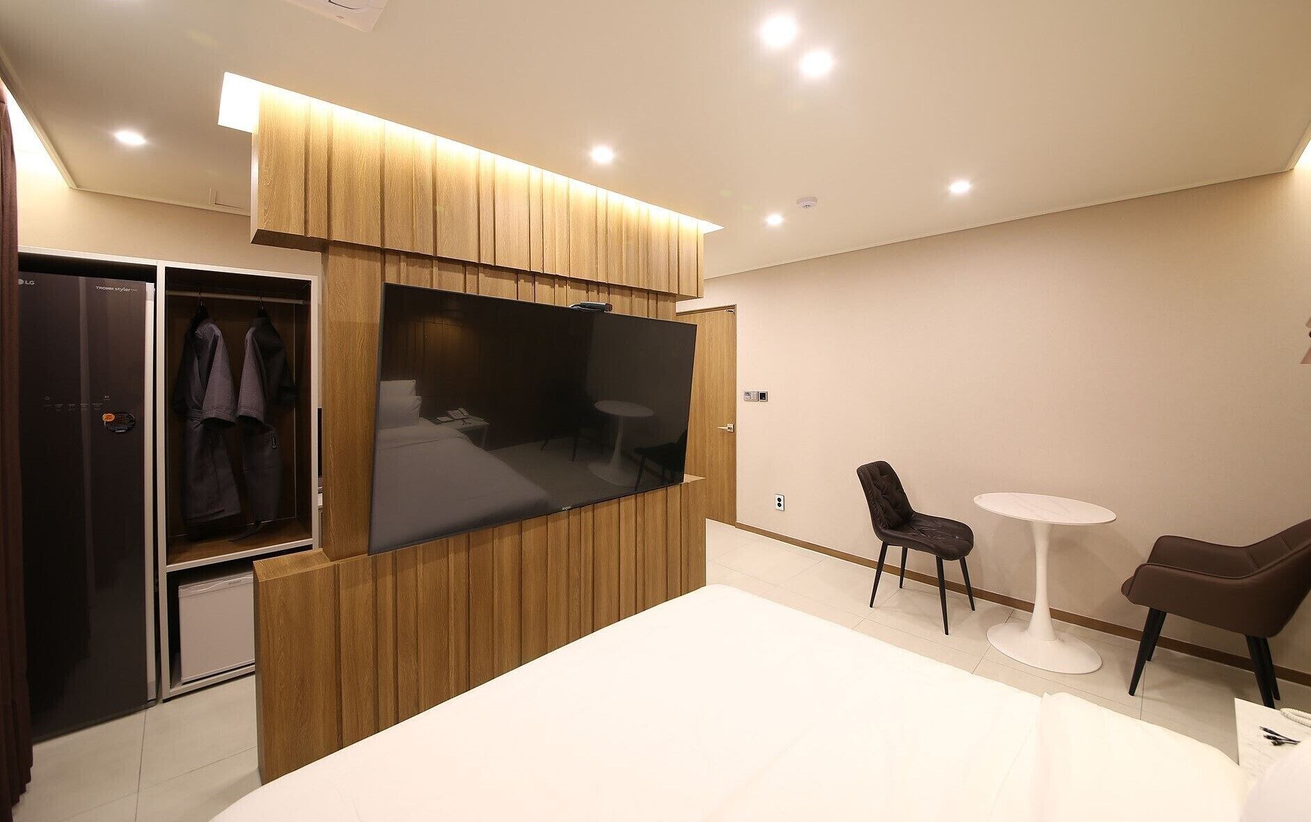 Une chambre d’hôtel moderne équipée d’un placard, d’un lit, d’une télévision et d’un coin salon avec deux fauteuils et une petite table.