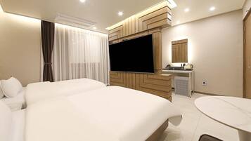 Habitación de hotel con dos camas, televisor, kitchenette pequeño y una mesa de comedor redonda.