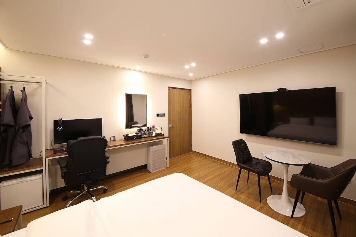 Una habitación de hotel con cama, escritorio, silla, televisor y una mesita.