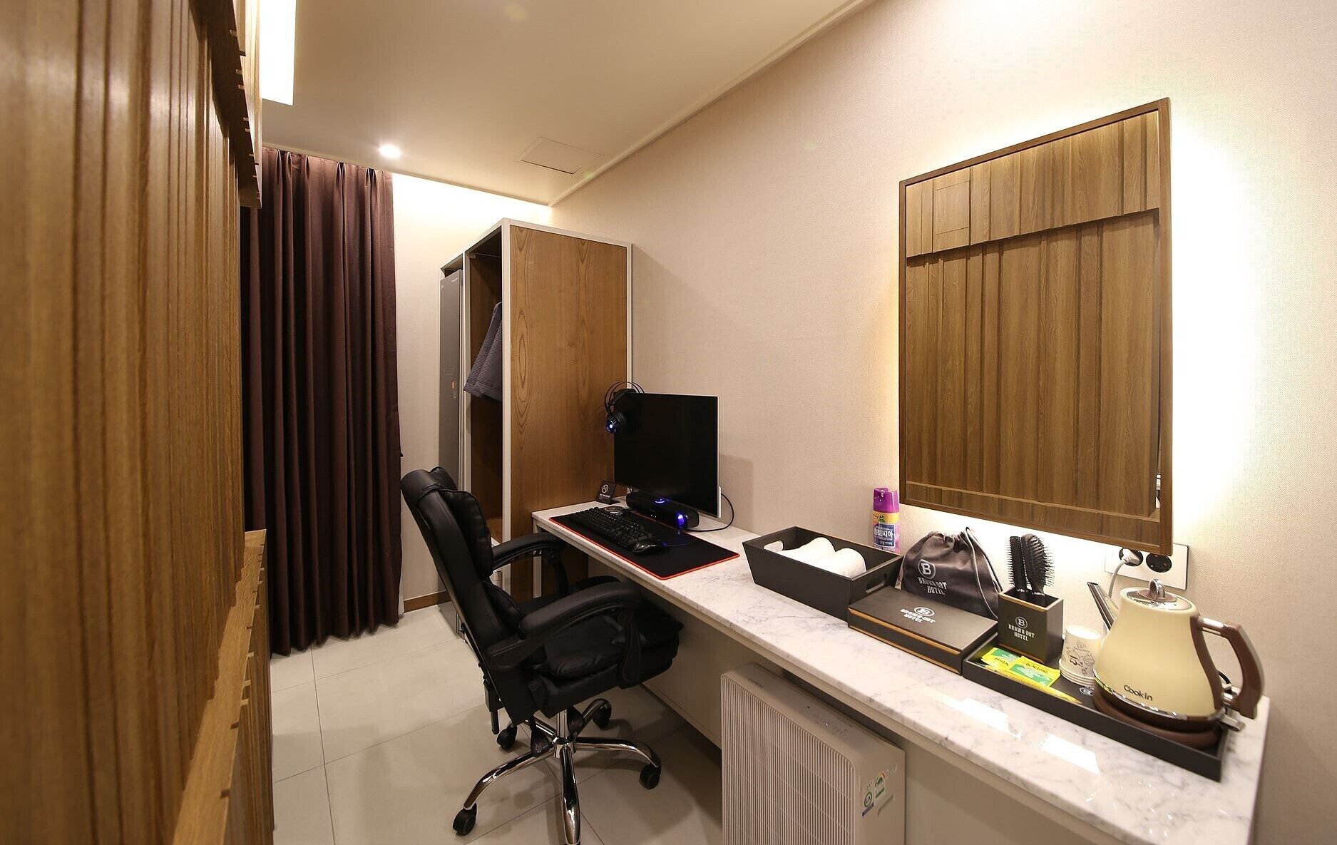 A hotel room with a desk, computer, chair, and a minibar.
