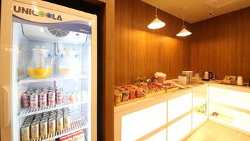 A minibar with a UNICOOLA refrigerator stocked with beverages and snacks, a coffee machine, and a counter with various food items.