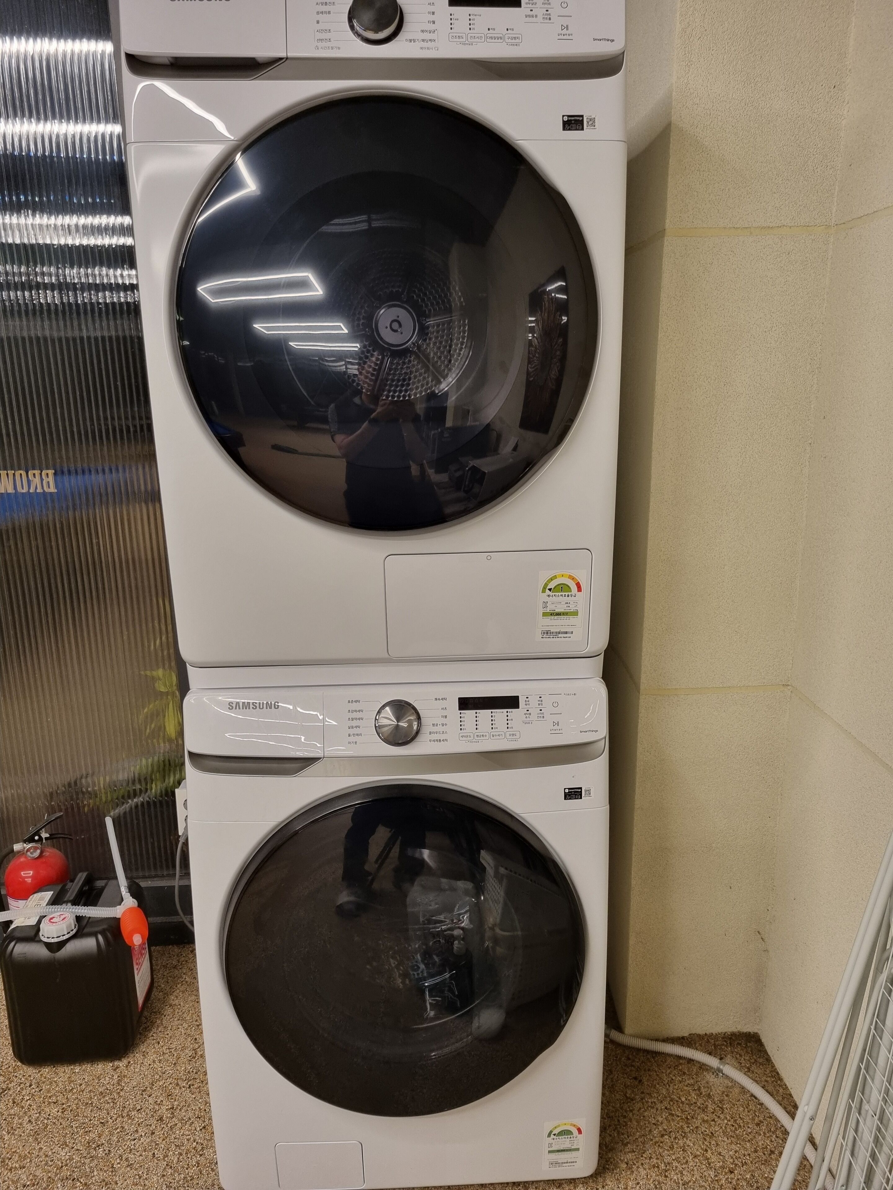 Een gestapelde wasmachine en droger met een bedieningspaneel, een veiligheidsslot en een watertoevoerslang.