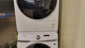 Een gestapelde wasmachine en droger met een bedieningspaneel, een veiligheidsslot en een watertoevoerslang.