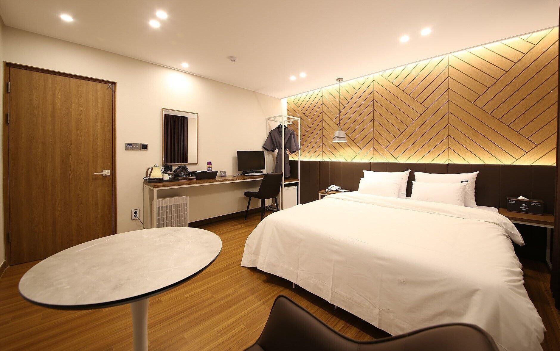 Habitación de hotel con cama, escritorio con computadora, silla, mesita y armario.