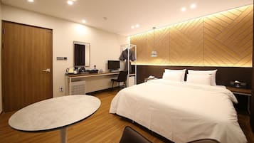 Habitación de hotel con cama, escritorio con computadora, silla, mesita y armario.