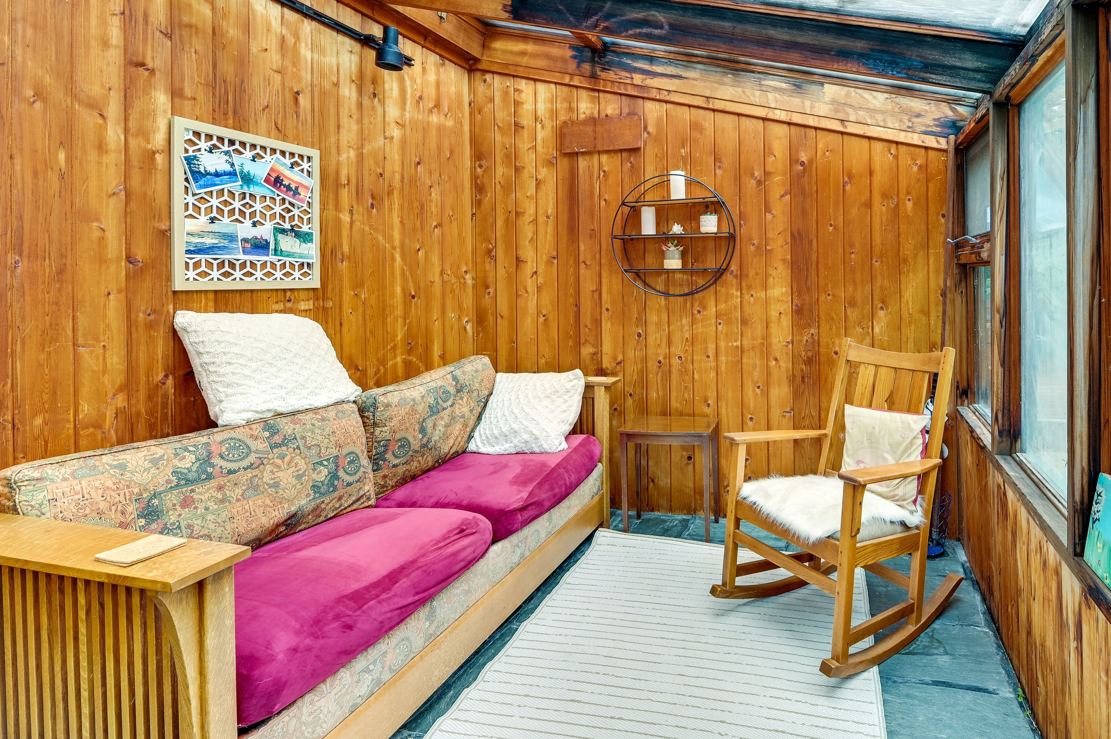 Interior de una cabaña de madera con sofá, sillón mecedor y estante en la pared.