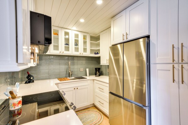 A modern kitchen with white cabinets, a stainless steel refrigerator, and a black countertop. - New Smyrna Beach Condo: Pool Access, Walk to Beach (New Smyrna Beach)