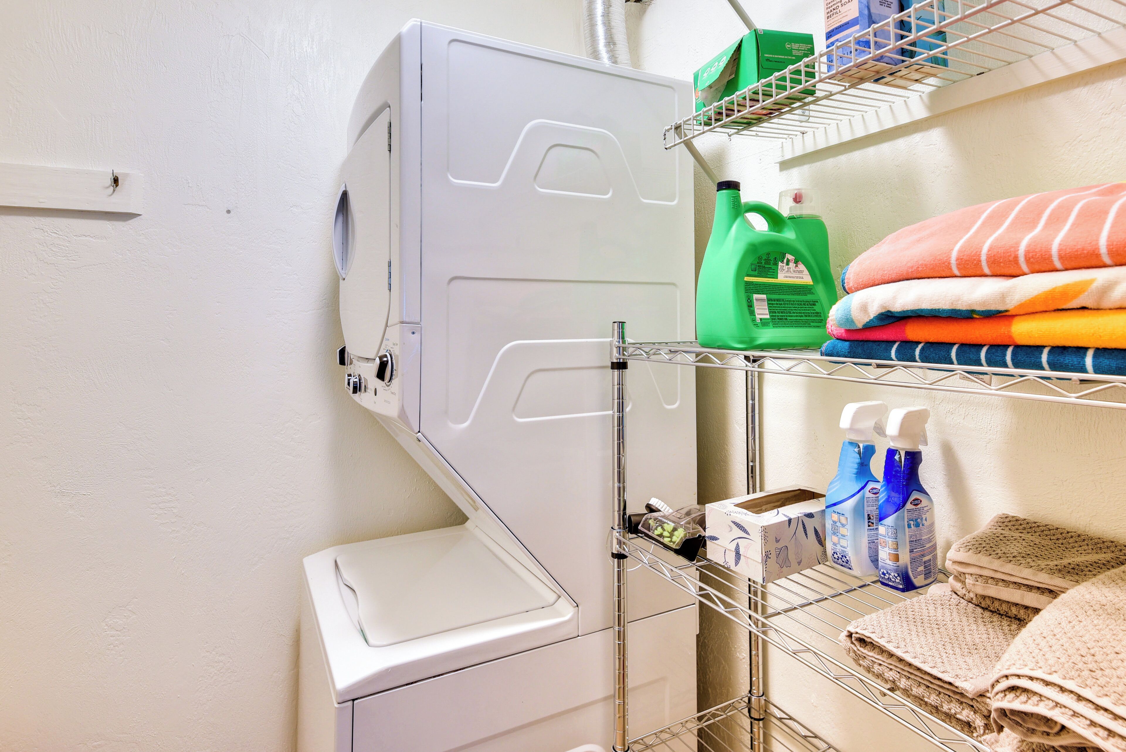 Een wasruimte met een wasmachine, planken met opgevouwen handdoeken en schoonmaakspullen.
