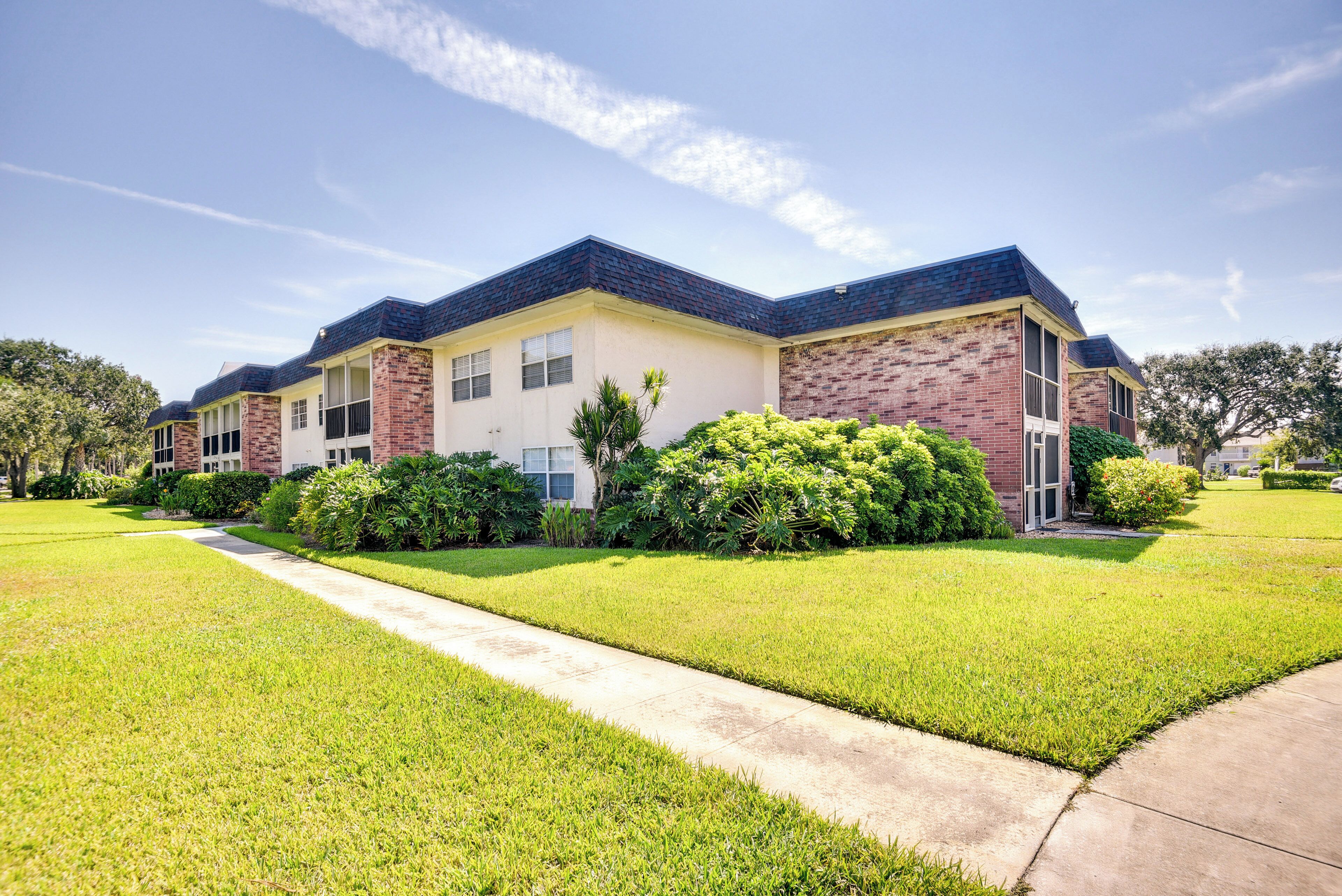 A two-story residential building with a brick facade, large windows, and a well-maintained lawn.