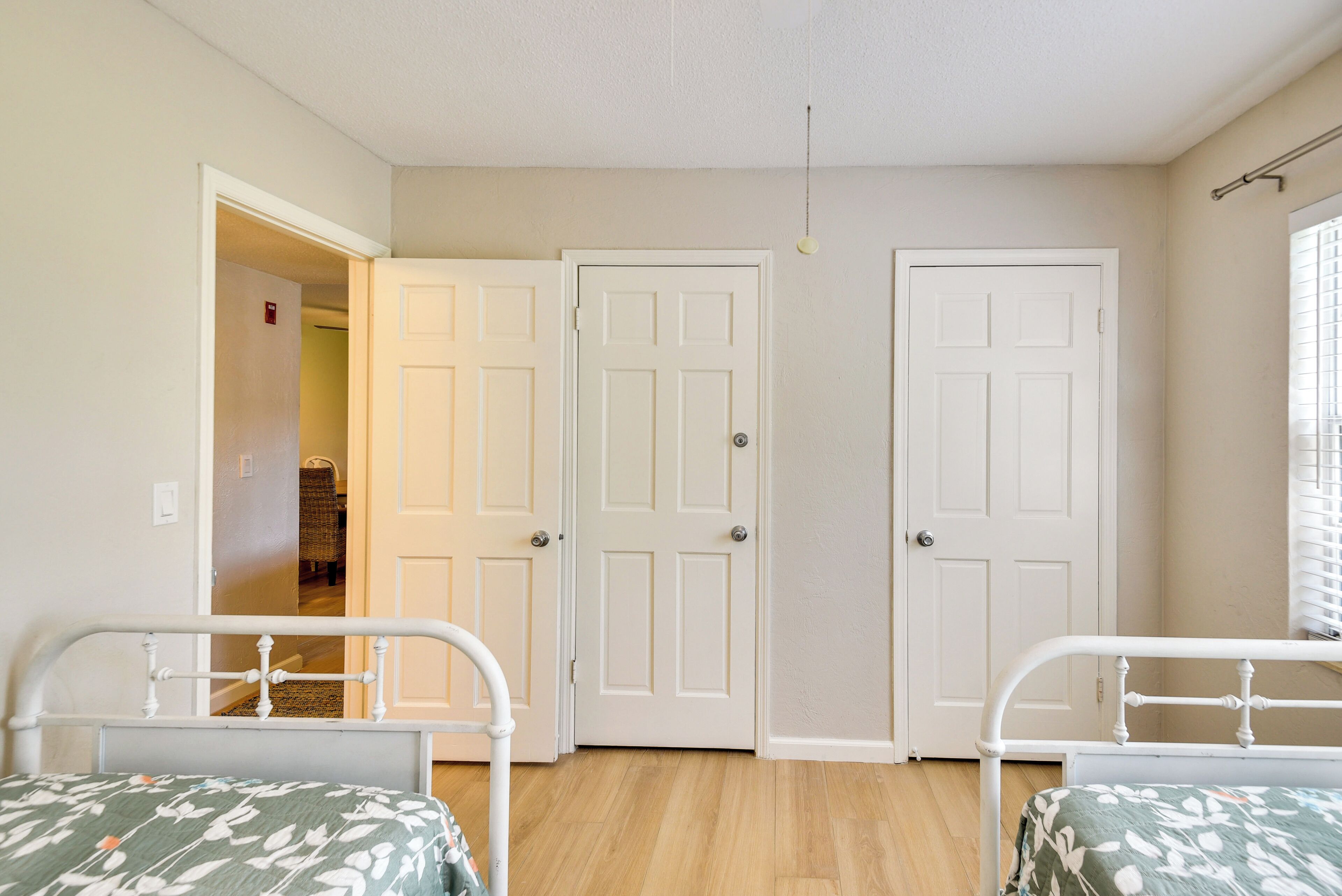 A bedroom with two single beds, a door, and a hallway leading to another room.