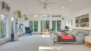 A spacious bedroom with a large bed, a desk, and a chair. There are multiple windows providing natural light and views of the outdoors. - Charming Thornton Escape w/ Sauna + Gazebo! (Thornton)