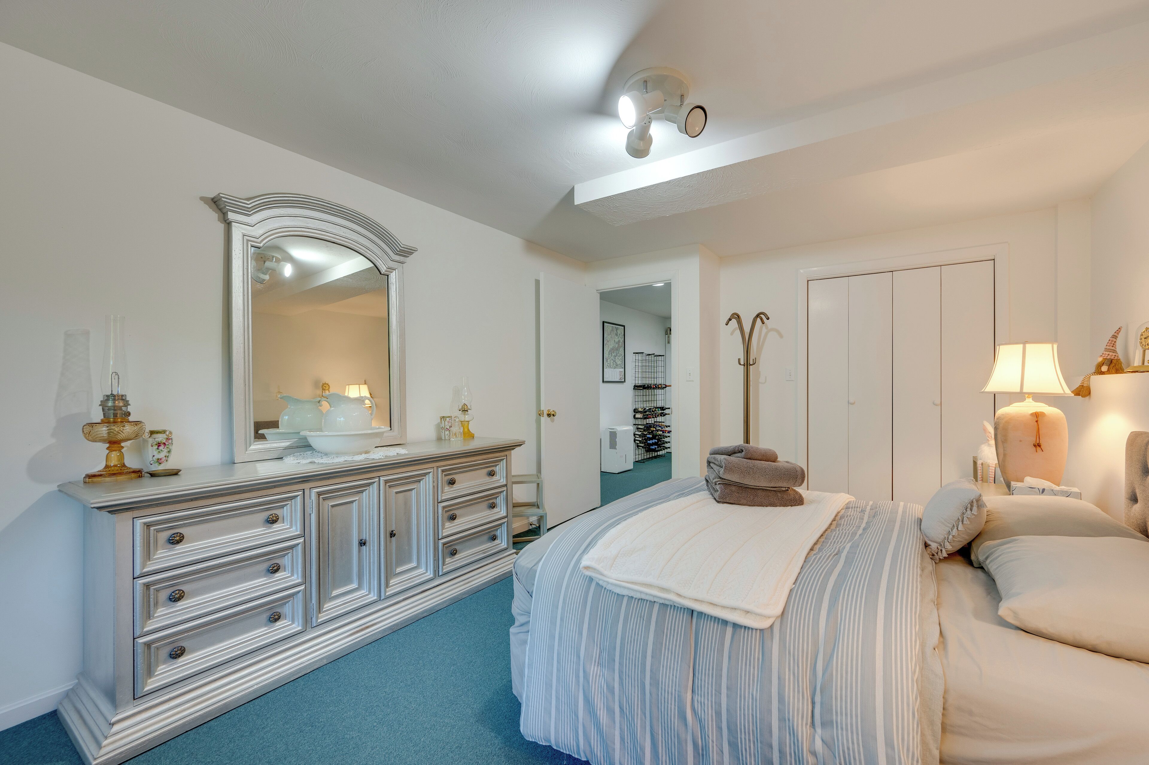A bedroom with a large bed, a dresser, a mirror, and a door leading to a bathroom.
