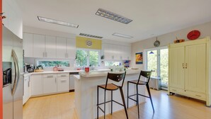 A modern kitchen with white cabinets, a central island with stools, and a large window providing natural light. - Charming Thornton Escape w/ Sauna + Gazebo! (Thornton)