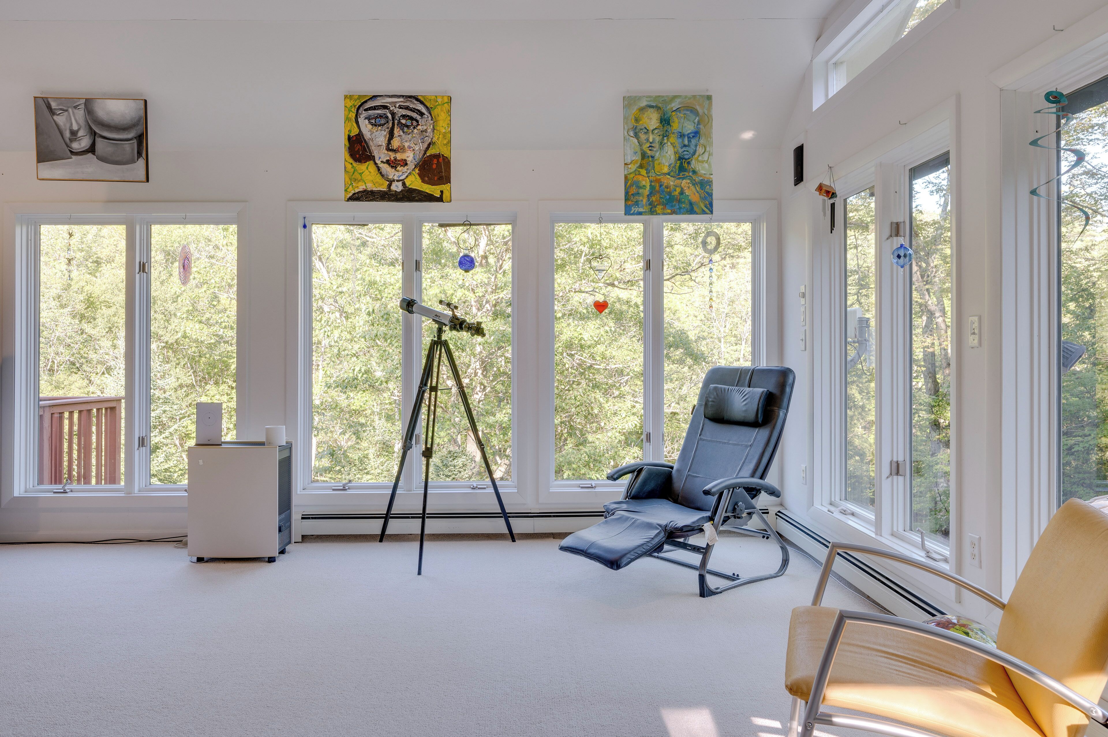 A room with large windows, a reclining chair, a telescope, and artwork on the walls.