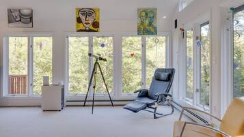 A room with large windows, a reclining chair, a telescope, and artwork on the walls.