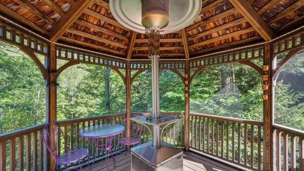 A covered wooden deck with a central heater, a table, and two chairs. - Charming Thornton Escape w/ Sauna + Gazebo! (Thornton)