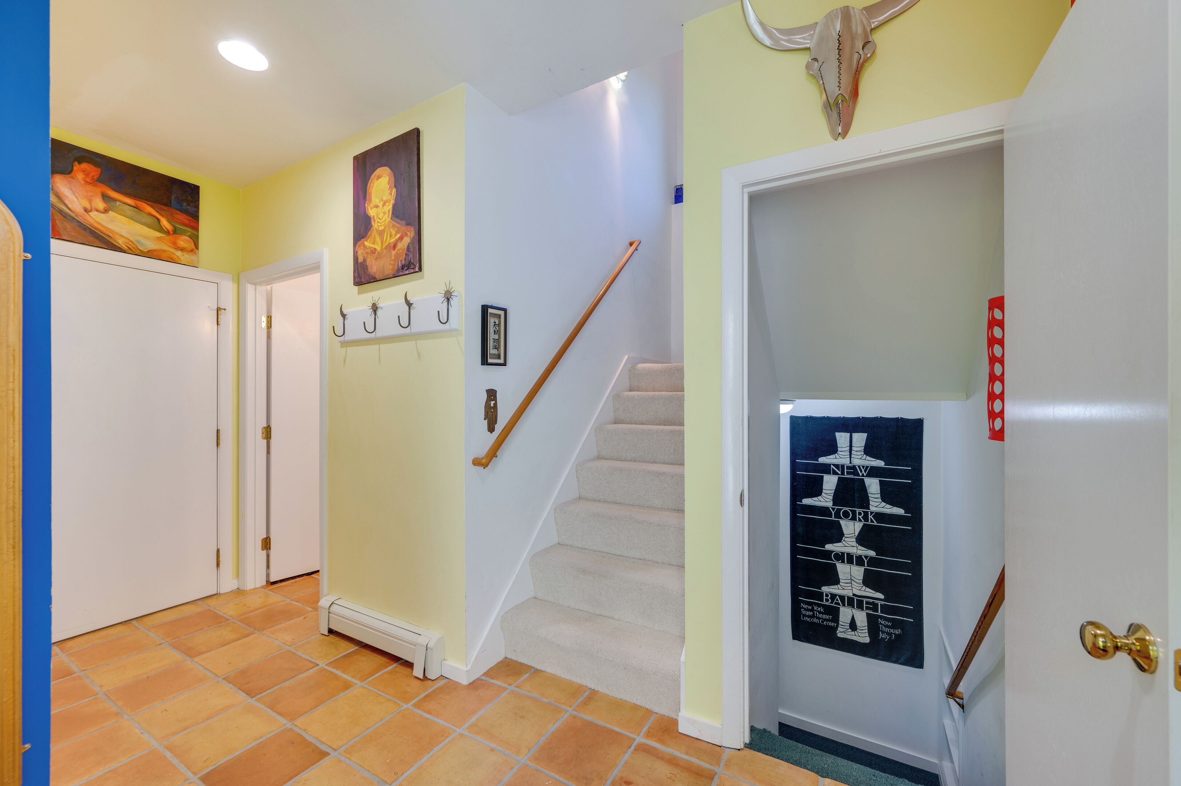 Un couloir avec un escalier, une porte ornée d’une affiche et un mur décoré d’un motif représentant un crâne.