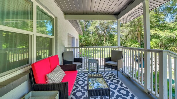 A covered porch with wicker furniture, a red sofa, and a patterned floor.