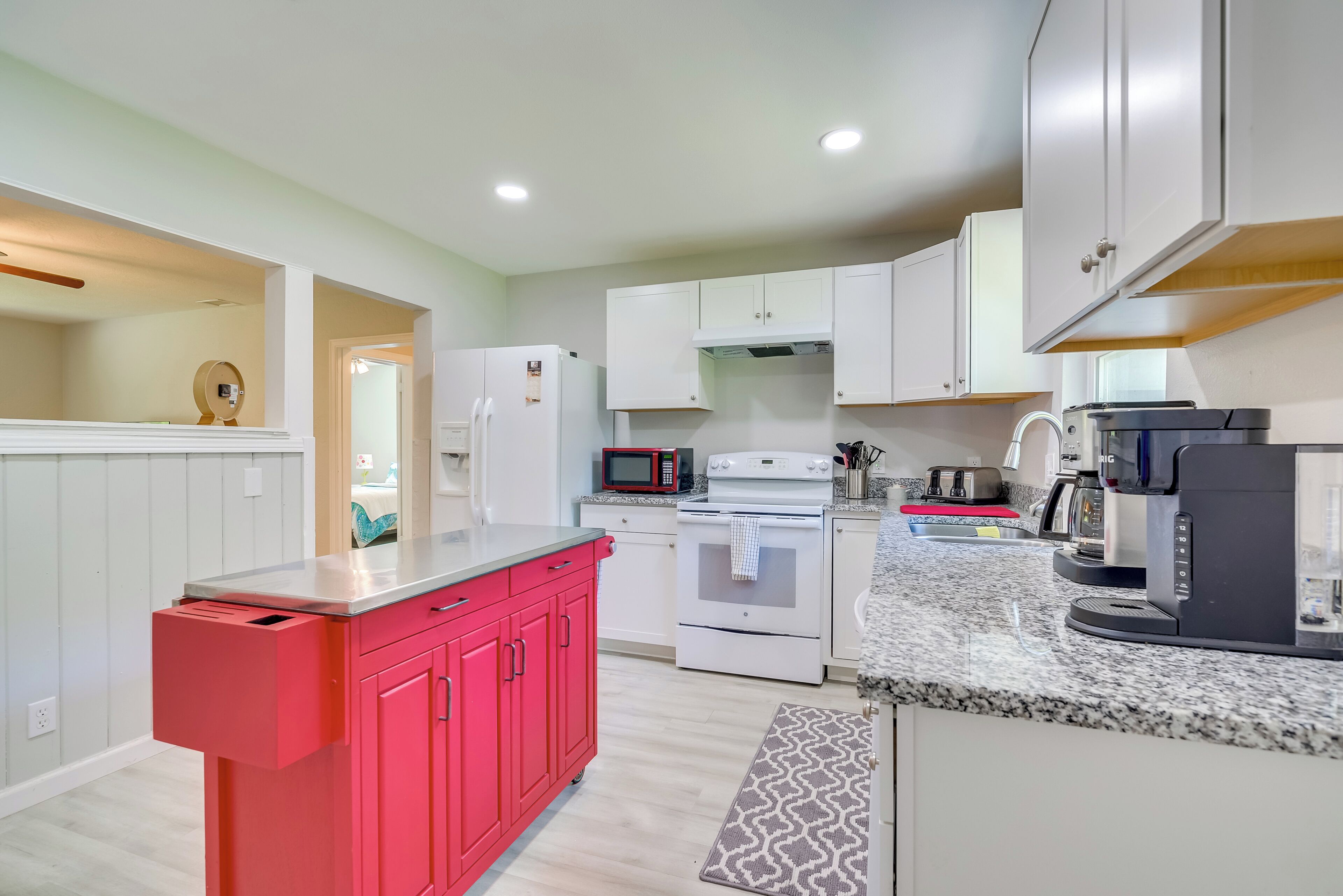 A modern kitchen with white cabinets, a red countertop, and a built-in microwave.