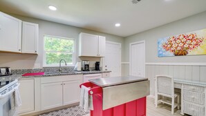A modern kitchen with white cabinets, a red island, and a painting of flowers on the wall.