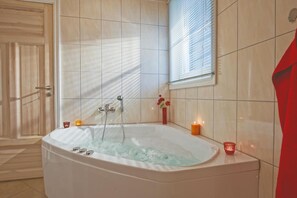 A bathroom with a large bathtub, tiled walls, a window with blinds, and candles on the floor. - Großzügiges Ferienhaus in Bad Saarow (Bad Saarow)