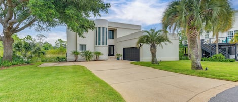 A modern house with a large driveway, palm trees, and a well-maintained lawn.