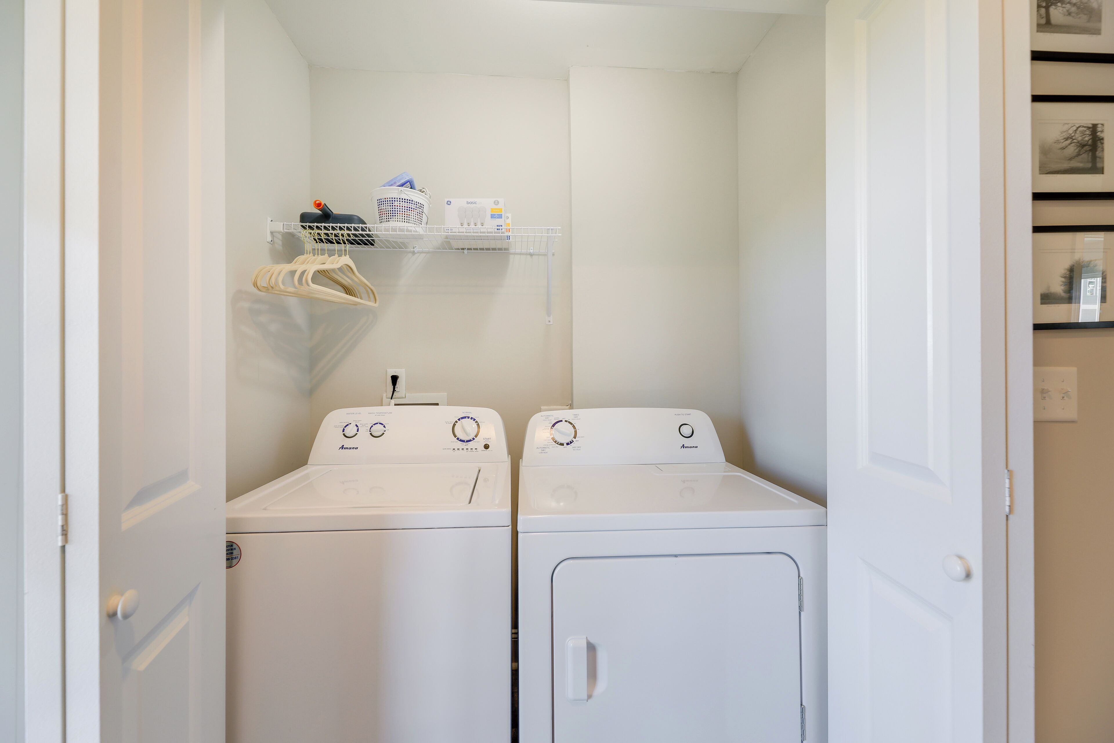 A laundry room with two white front-loading washing machines and a shelf above them holding a basket and some items.