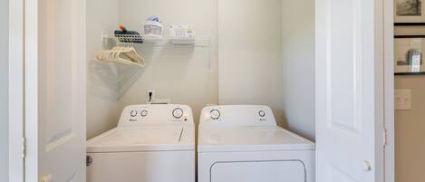 A laundry room with two white front-loading washing machines and a shelf above them holding a basket and some items.