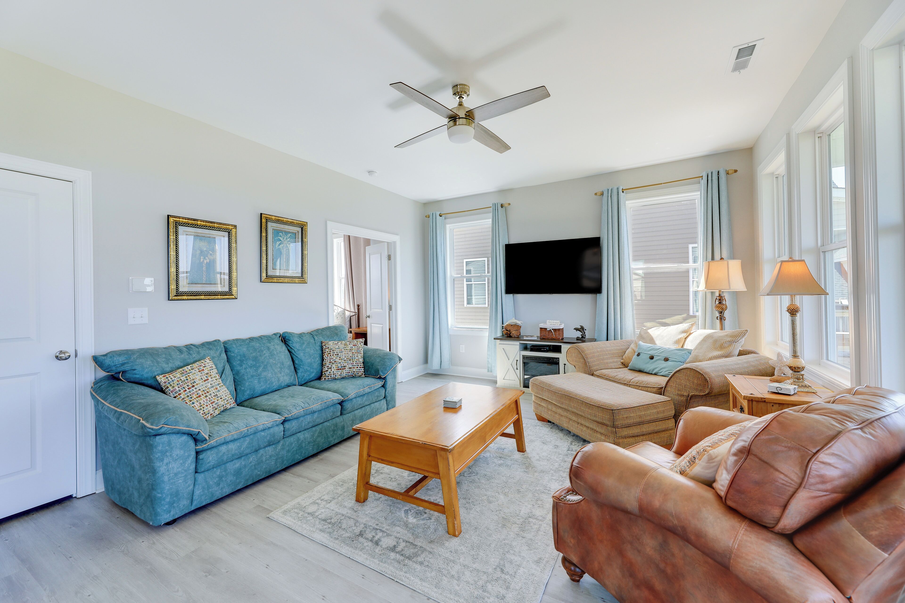 A living room with a blue sofa, a brown leather sofa, a wooden coffee table, and a ceiling fan.
