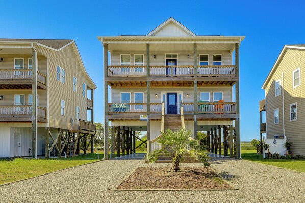 A multi-story building with a balcony on the second floor, a covered entrance, and a small palm tree in the foreground. - North Topsail Getaway w/ Panoramic Sound Views! (Sneads Ferry)