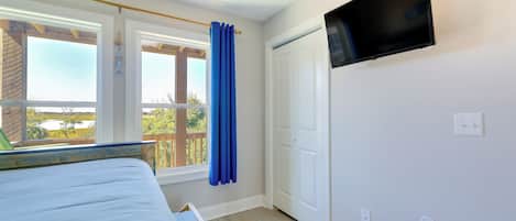 A bedroom with a bed, a TV mounted on the wall, a window with curtains, and a door.