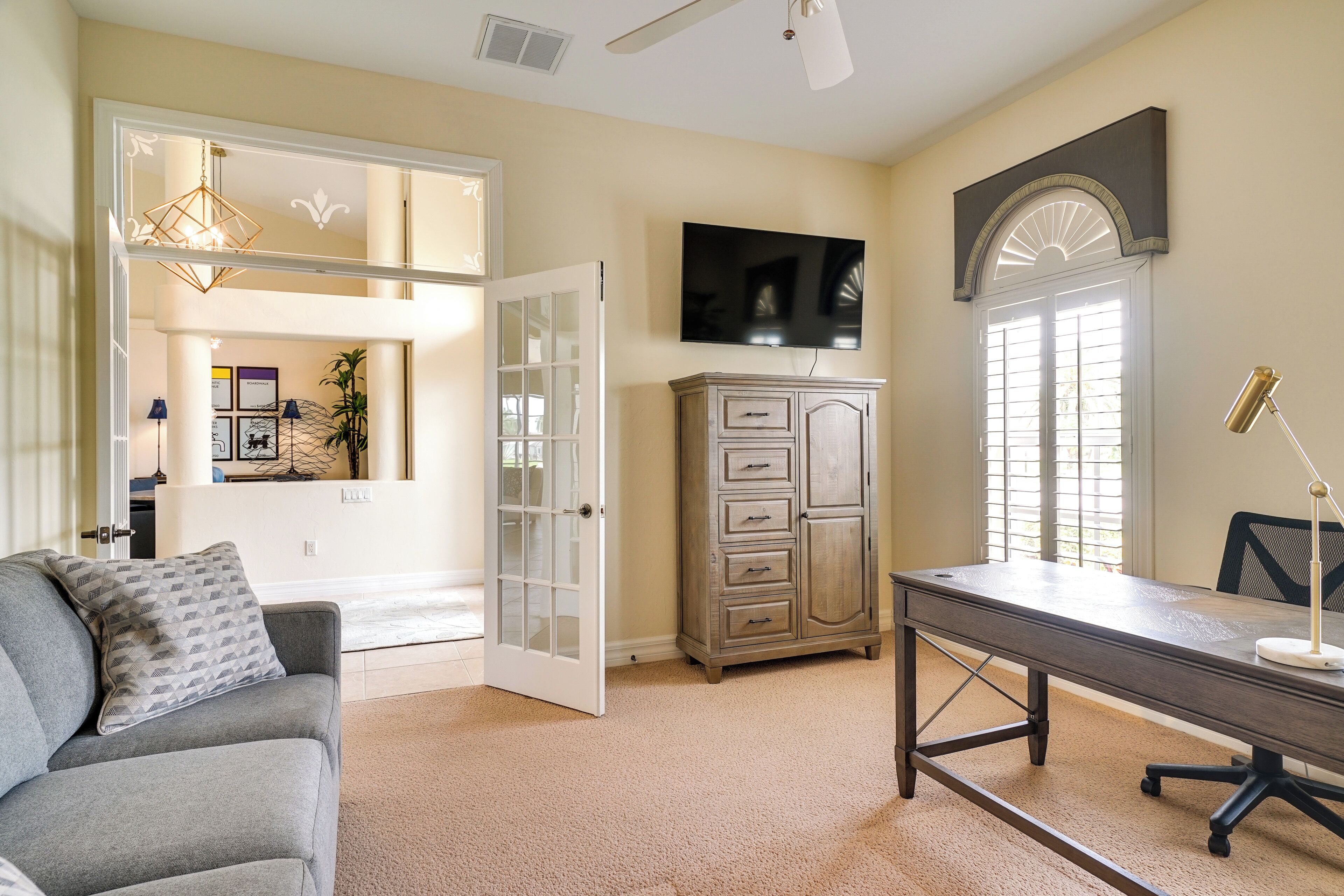 A room with a gray sofa, a desk, a cabinet, and a television on the wall.