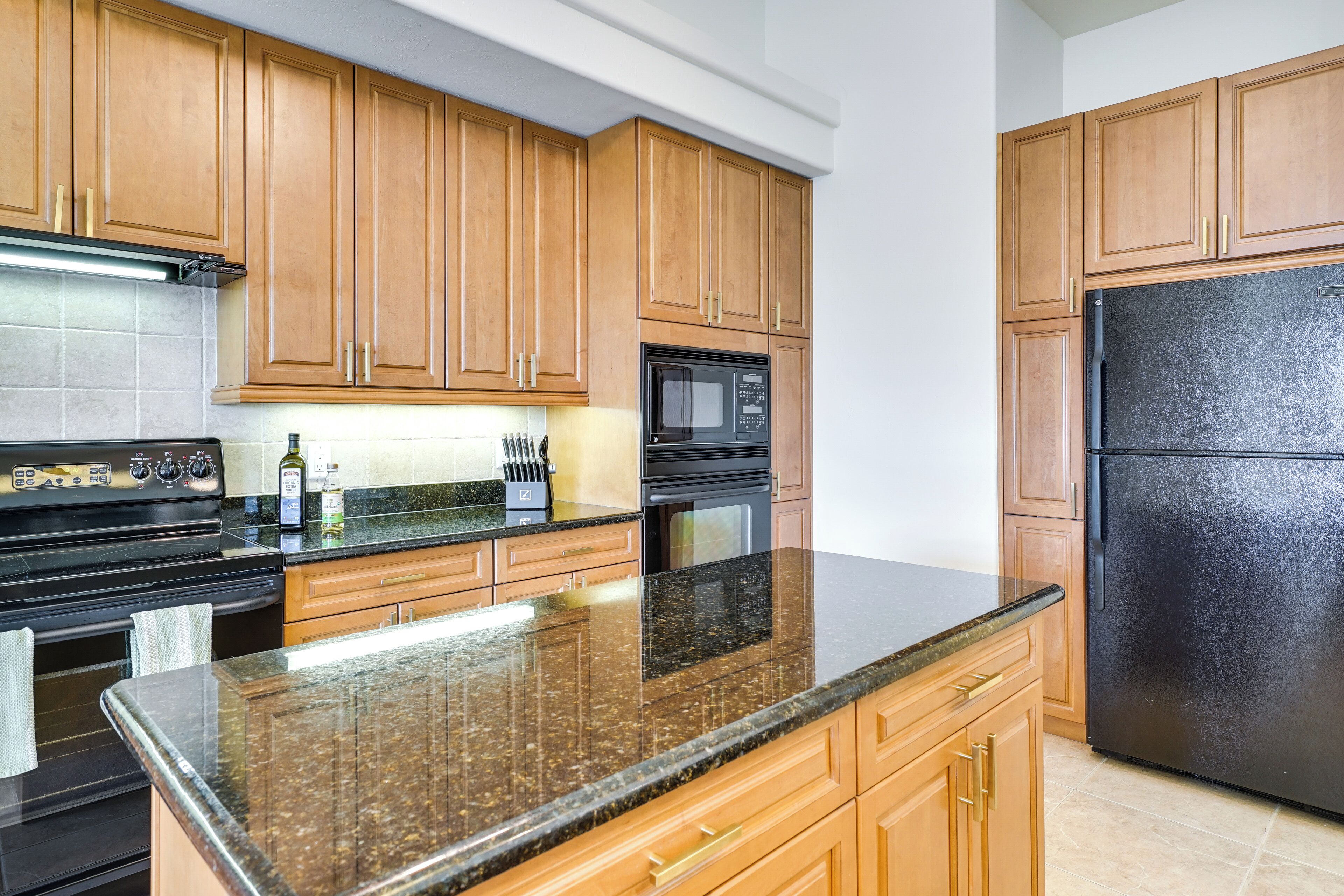 A kitchen with wooden cabinets, a granite countertop, a black refrigerator, and a black microwave.