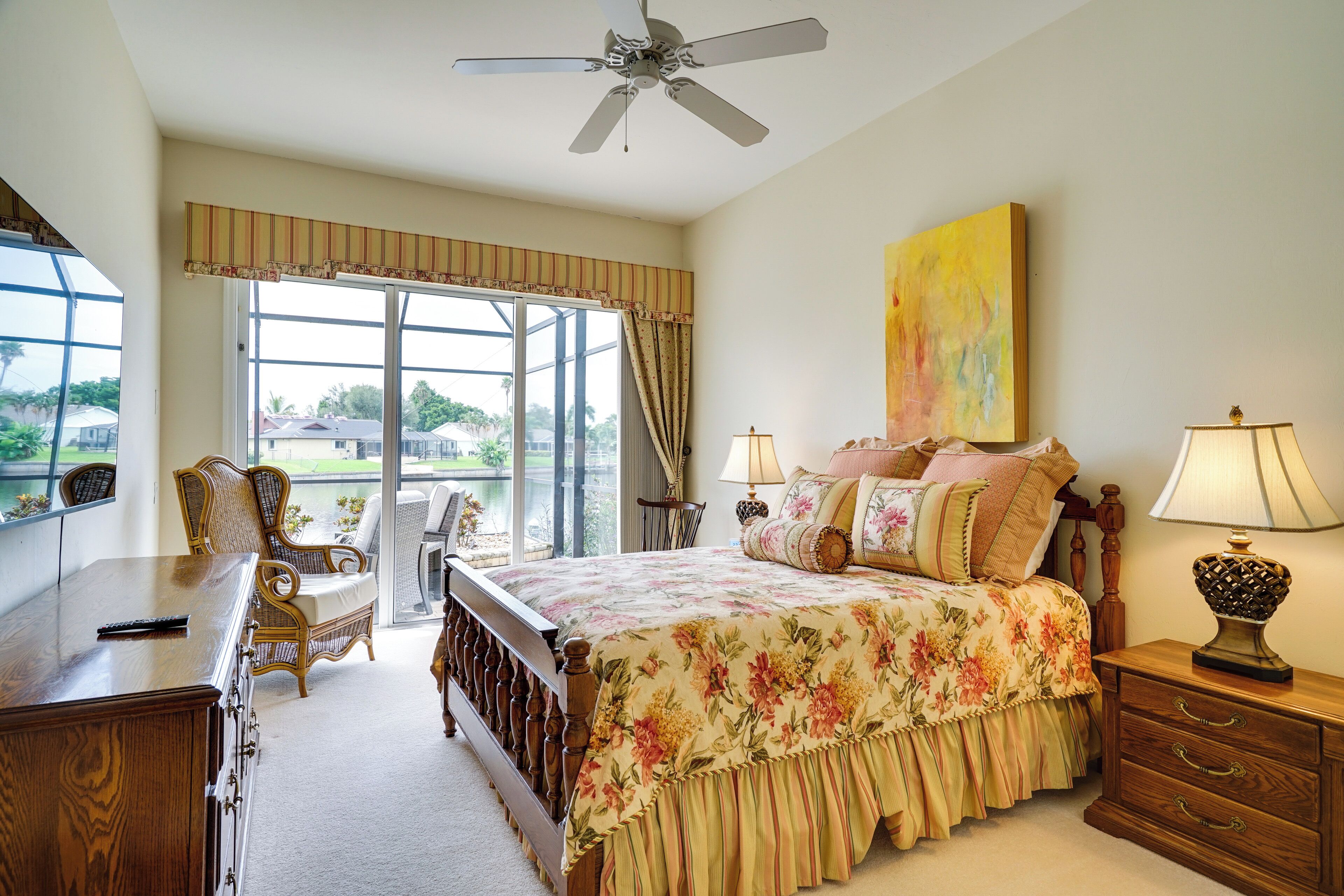 A bedroom with a large bed, a desk, a chair, a nightstand, and a ceiling fan.