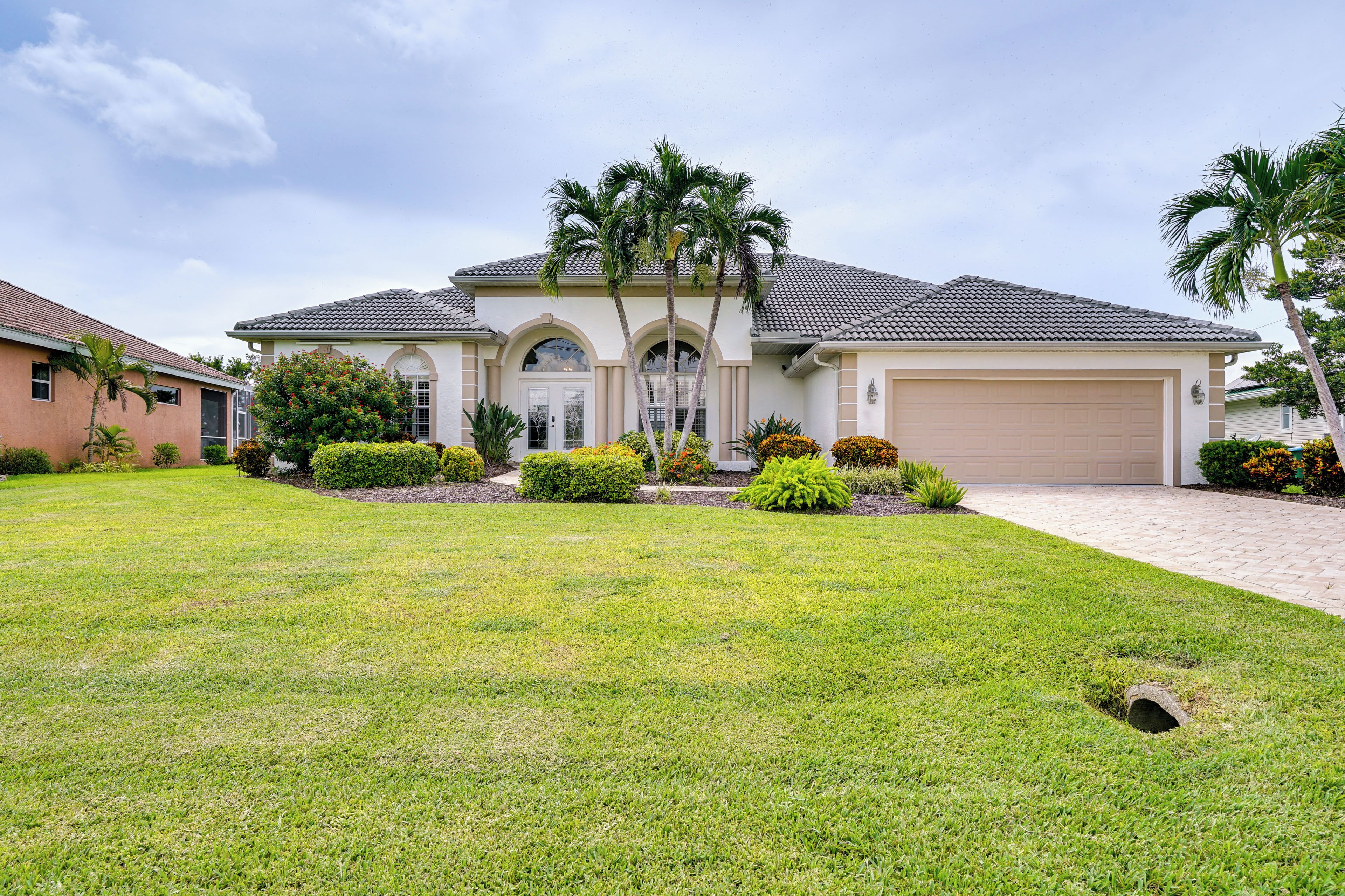 A two-story house with a garage, surrounded by well-maintained lawns and palm trees.