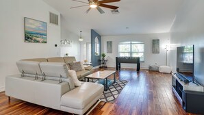 Ein geräumiges Wohnzimmer mit einem weißen Sofa, einem Couchtisch, einem Deckenventilator und einem großen Fenster.