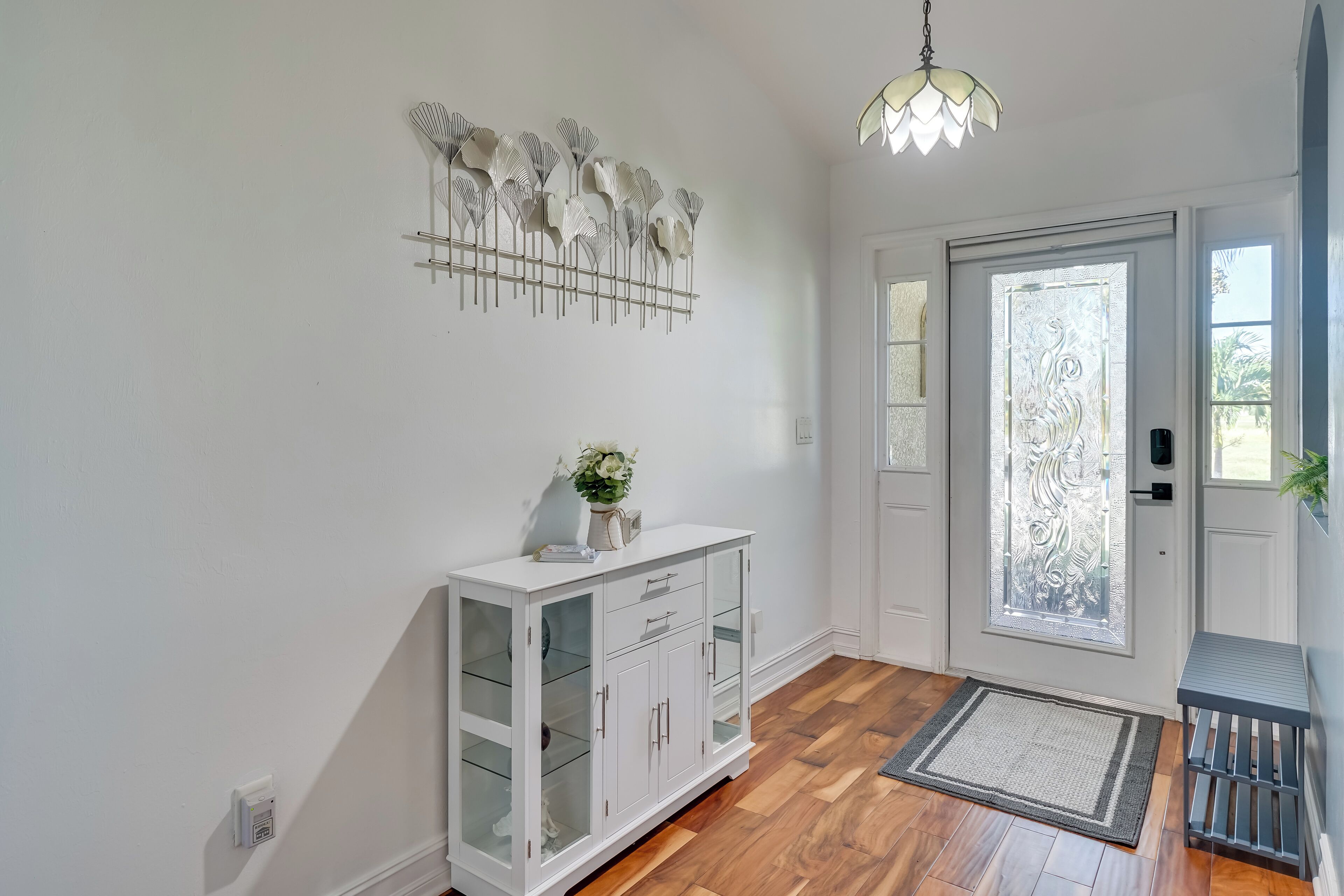 Een nette, moderne entree met een witte console, een decoratief wandobject en een houten vloer.