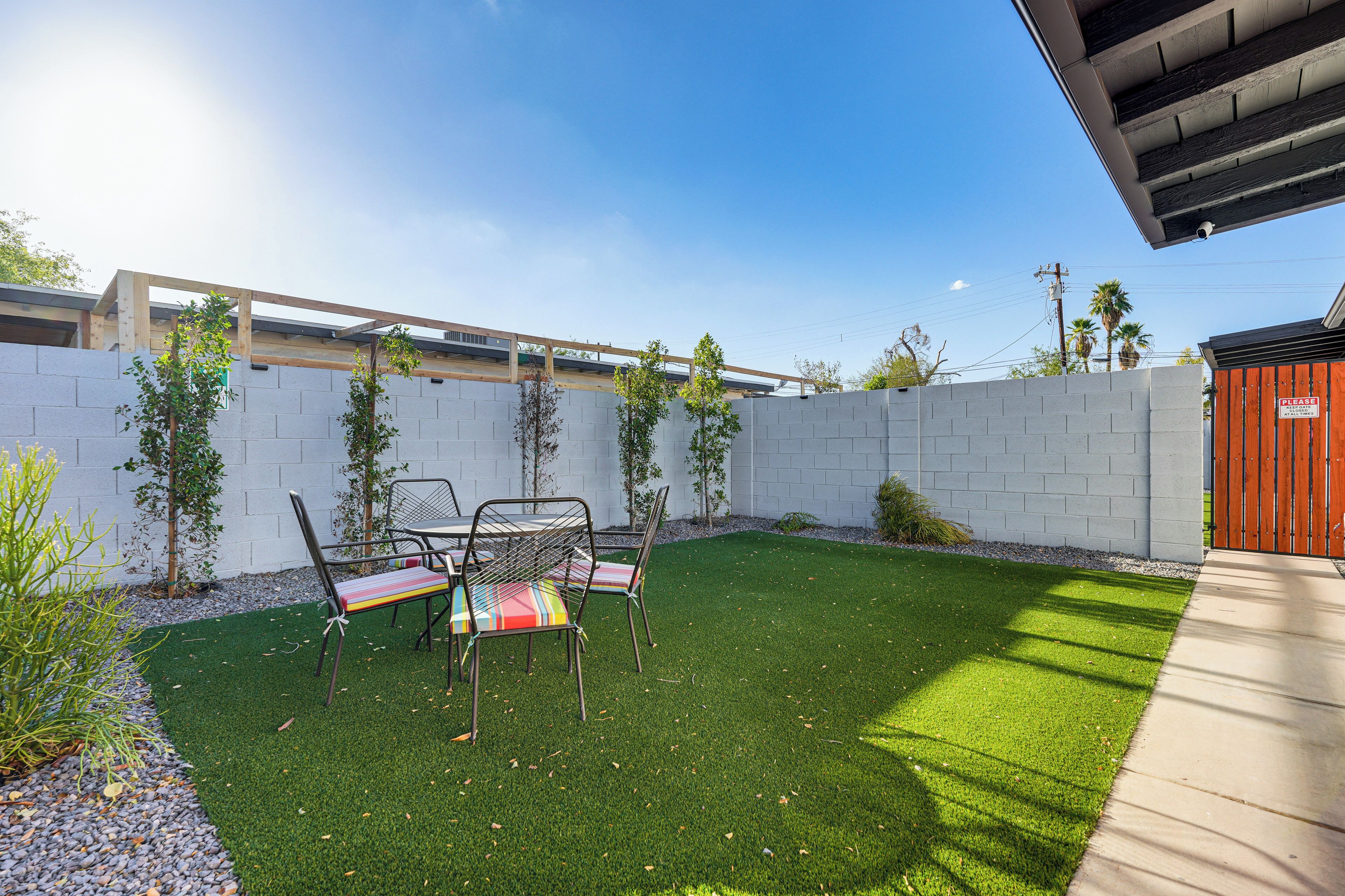 A backyard with artificial grass, a table and chairs, a wooden fence, and a red gate.