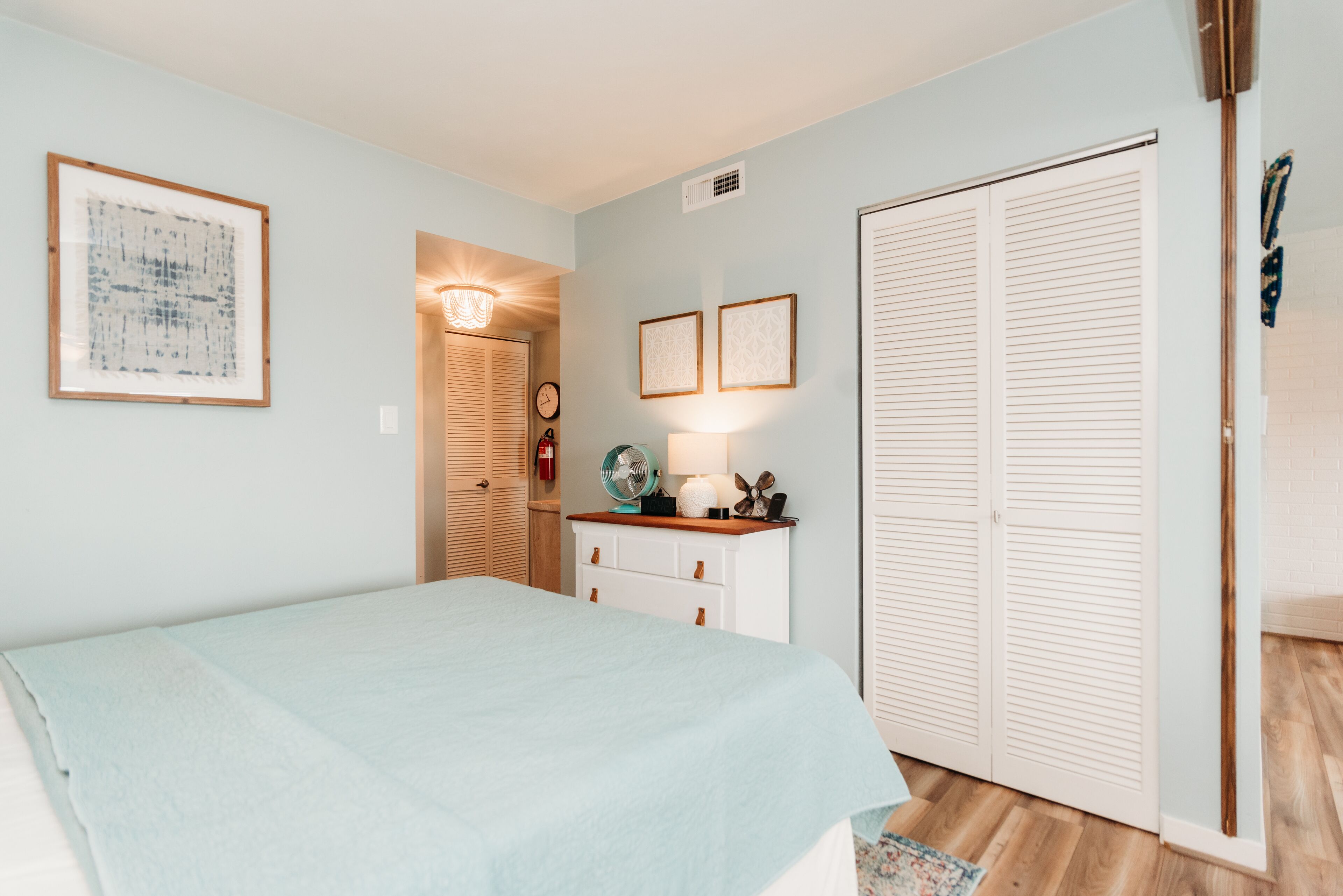 A bedroom with a bed, a dresser, a nightstand, a fan, and a closet.